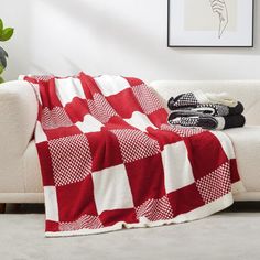 a red and white blanket sitting on top of a couch next to a potted plant