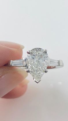 a woman's hand holding an engagement ring with a pear shaped diamond in the center