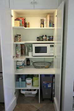 an open pantry with white cabinets and shelves filled with various items, including a microwave