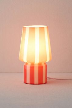 an orange and white striped lamp sitting on top of a table next to a wall