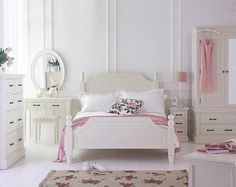 a bedroom with white furniture and flowers on the bed, dressers, mirror and rug