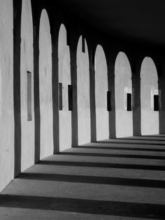 black and white photograph of an arched wall with concrete pillars in the center, lined by small windows