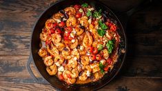 a skillet filled with shrimp and vegetables on top of a wooden table