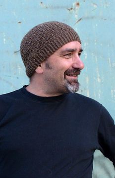 a man wearing a knitted hat standing in front of a blue wall