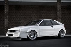 a white car parked in front of a brick wall