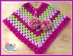 a pink and green crocheted square with a bow on the end, sitting on top of a wooden table