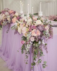 the table is covered with lavender colored flowers and greenery as well as white candles