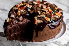 a chocolate cake on a white plate with a slice taken out of it and the rest of the cake is covered in candy