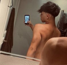 a shirtless man taking a selfie in front of a mirror with his cell phone