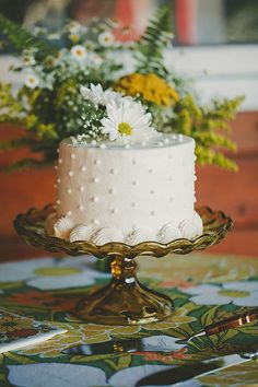 a white cake sitting on top of a glass plate next to flowers and greenery