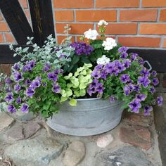 a metal bucket filled with purple and white flowers sitting next to a brick wall in front of a door