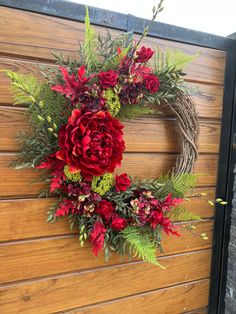 a wreath with red flowers and greenery hanging on a wooden wall next to a door