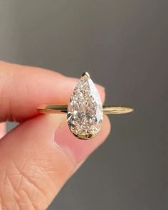 a woman's hand holding a yellow gold ring with a pear shaped diamond