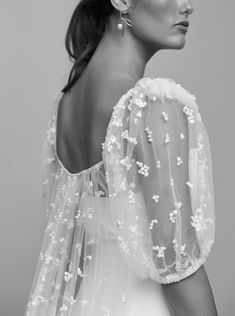 a woman in a white dress with flowers on her back and veil over her shoulder