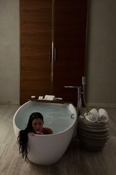 a woman sitting in a bathtub next to stacks of towels