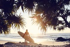 a woman holding a surfboard on top of a sandy beach