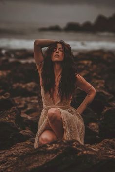 a woman sitting on top of rocks near the ocean with her hands behind her head