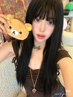 a woman with long black hair holding a teddy bear keychain in front of her face