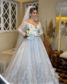 a woman in a wedding dress standing next to a couch and holding a bouquet of flowers