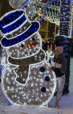 a woman standing next to a snowman with lights on it's face and head