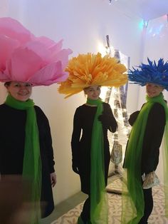 three girls wearing hats and scarves with flowers on their heads are standing in front of a mirror