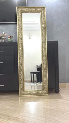 a large gold framed mirror sitting on top of a wooden floor next to a dresser