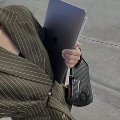 a woman holding an ipad in her right hand while wearing a suit and carrying a purse