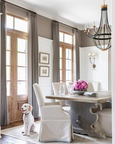 a dog sitting in front of a dining room table with chairs and a chandelier