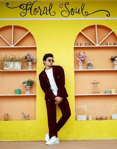 a man standing in front of a yellow wall wearing a red suit and white shirt