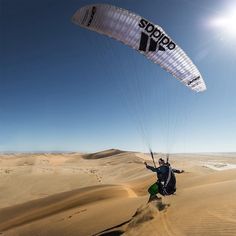 a man is parasailing in the desert with sand dunes and bright sun behind him