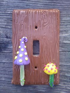 a brown light switch cover with two colorful mushrooms on it and a mushroom figurine next to it