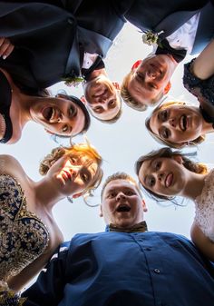 a group of people standing in a circle looking up at the camera with their hands together