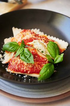 a black plate topped with pasta covered in sauce and spinach sprinkles