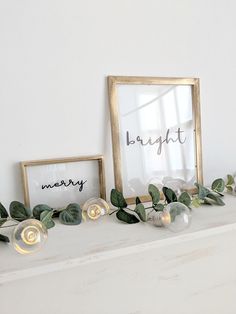 two framed pictures sitting on top of a white mantle next to eucalyptus leaves and candles