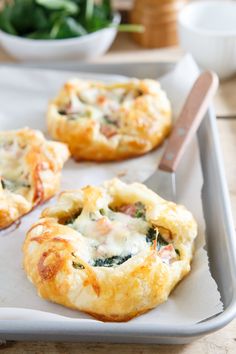 three mini pizzas sitting on top of a baking sheet next to a bowl of spinach