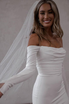 a woman wearing a white wedding dress with a veil on her head and smiling at the camera