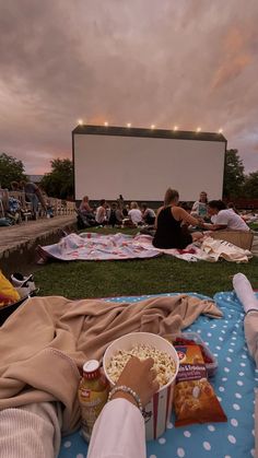 people sitting on the grass watching movies at an outdoor movie theater with popcorn and drinks