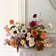 a vase filled with lots of different colored flowers on top of a marble table next to a mirror