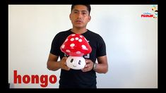 a man holding a red mushroom toy in front of a white wall with the words hello kitty on it