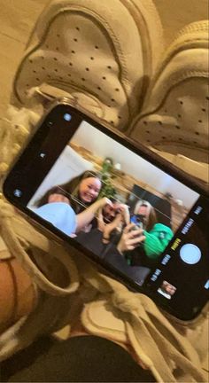 someone holding up their cell phone to take a selfie with two other people in the background