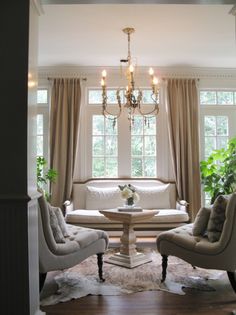 a living room filled with furniture and a chandelier hanging from the ceiling over a table