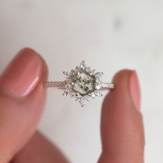 a woman's hand holding a ring with a green stone in the middle and white diamonds around it