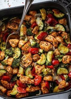 a pan filled with chicken and veggies on top of a table next to a spoon