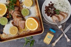 two plates with meat, rice and oranges on them next to a knife and fork