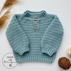 a crocheted sweater with buttons on the collar and sleeves, next to some yarn balls