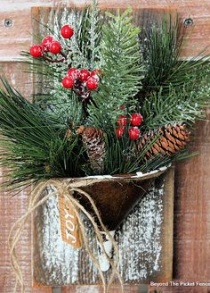 a wooden box with pine cones, berries and evergreen branches in it is hung on a wall