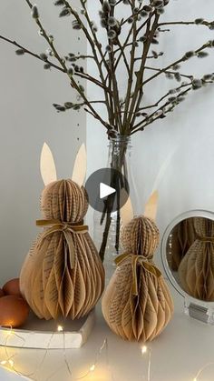 two paper rabbits sitting on top of a table next to a vase filled with eggs