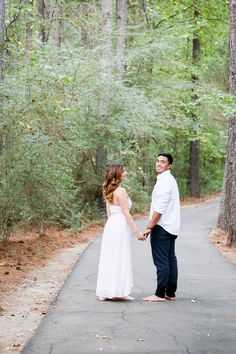 a man and woman holding hands while standing in the middle of a path surrounded by trees