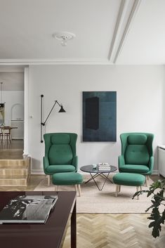 a living room with two chairs and a coffee table in front of a painting on the wall