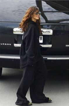 the woman is walking in front of her car wearing sunglasses and a black sweatshirt with an oversize hoodie